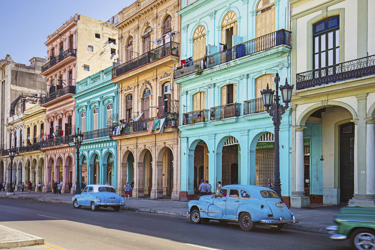 Straßenszene in Havanna, vor bunten Häusern stehen Autos aus den 50er Jahren