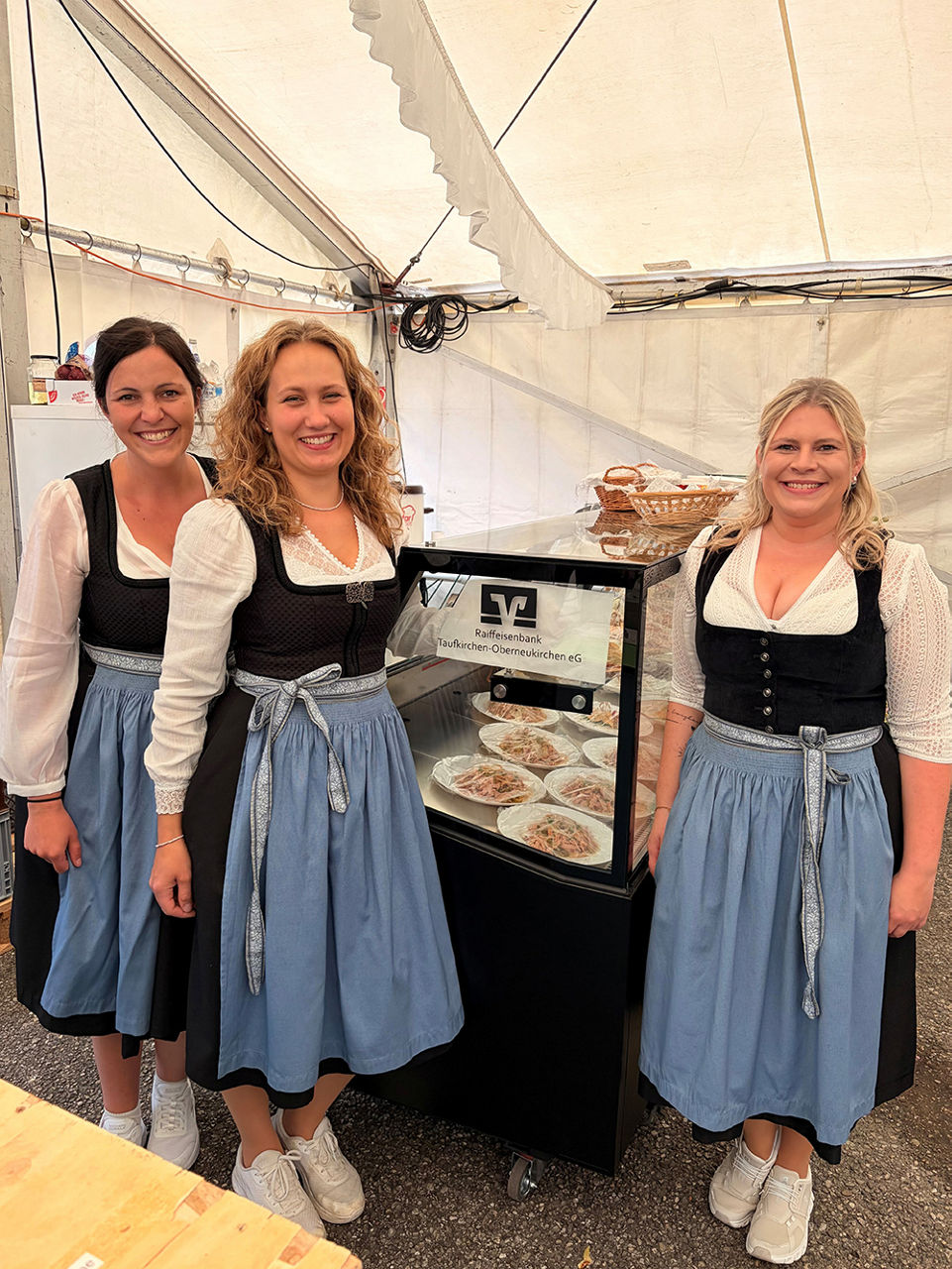 Drei Frauen im Dindl stehen vor einer Kühltheke
