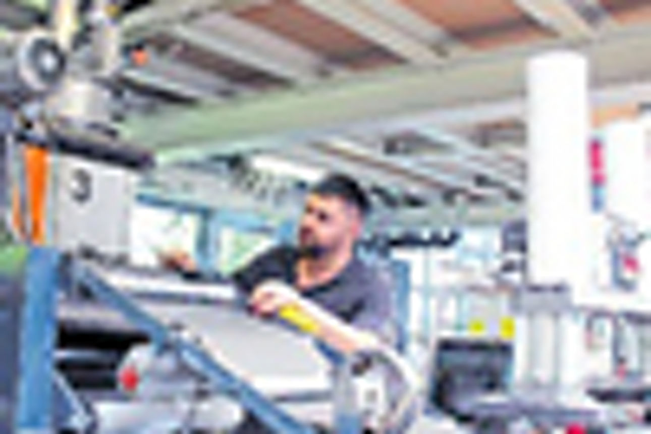 Ein Mann arbeitet an einer Maschine mit Zylindern, die Platten aus schwarzem Material herstellen