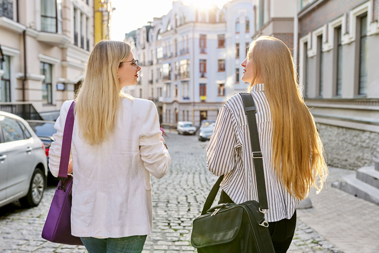 Rückenansicht zweier junger Frauen, die zu Fuß eine Straße entlang laufen