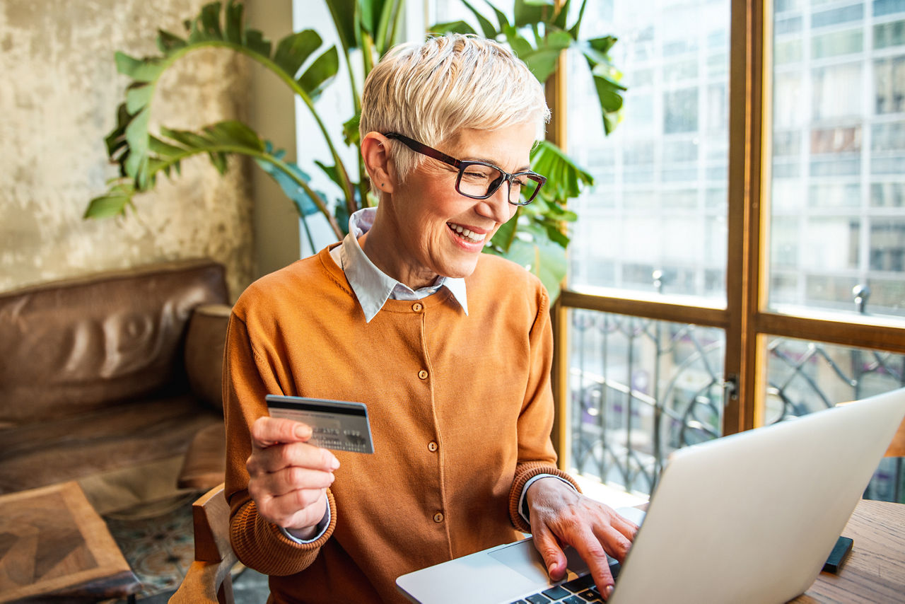 Frau sitzt mit Bankkarte in der Hand lächelnd vor einem Laptop