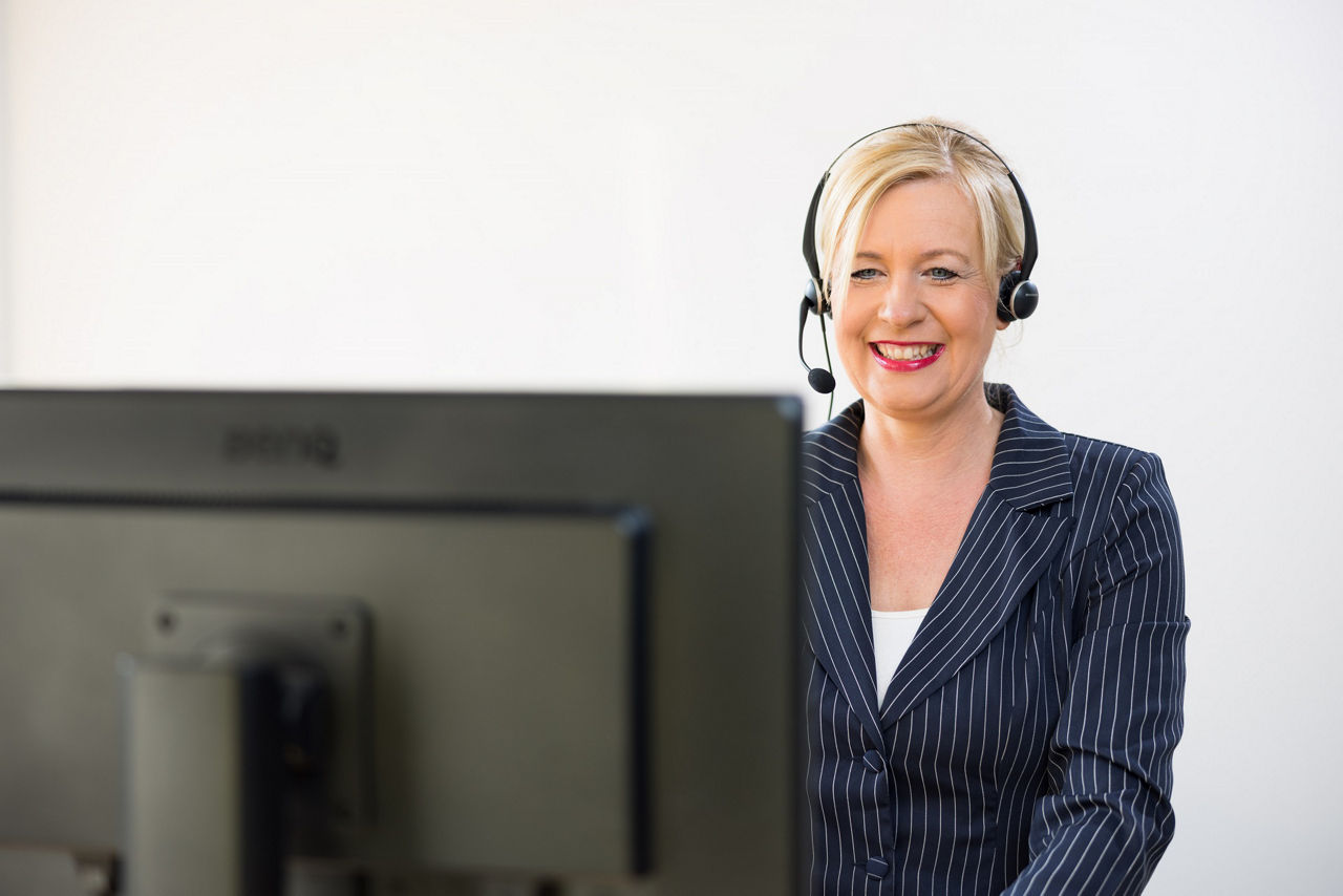 Bankmitarbeiterin mit Headset steht am Schreibtisch und arbeitet am PC.