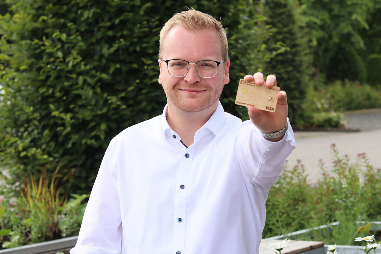 Privatkundenberater Linus Bröring mit einer Holz-Girocard in der Hand.
