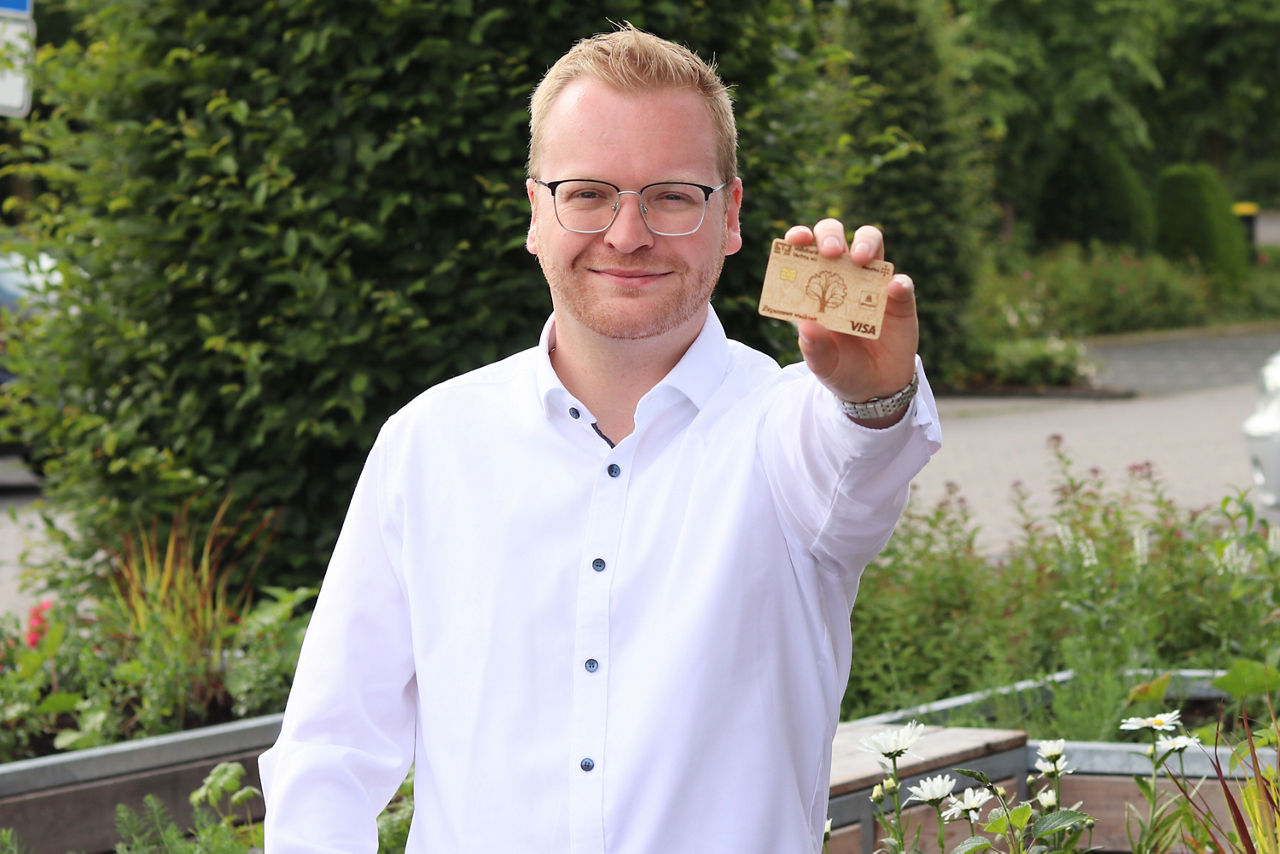 Privatkundenberater Linus Bröring mit einer Holz-Girocard in der Hand.