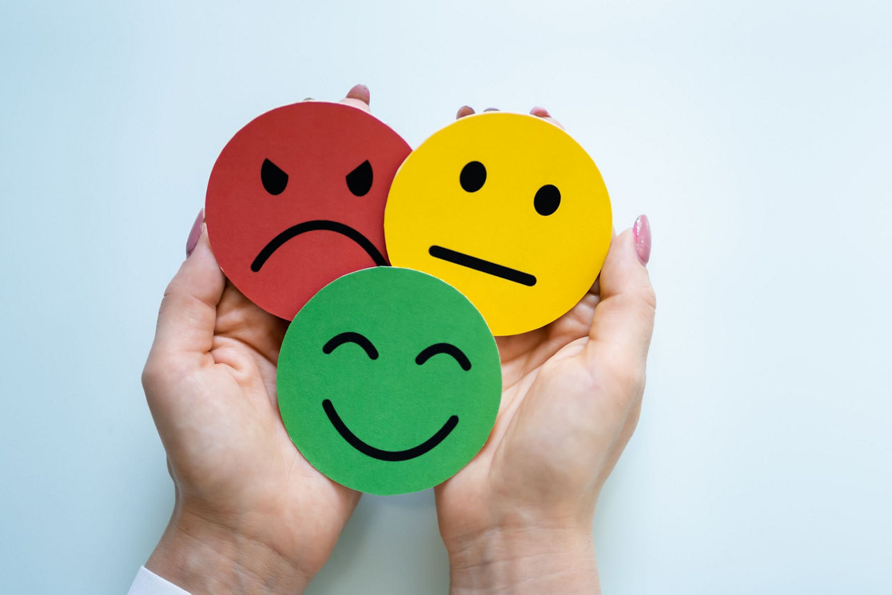 Zwei Hände halten drei Smileys, die erfreut, verärgert und neutral schauen