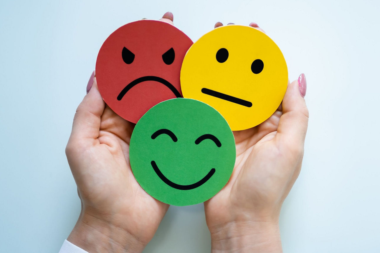 Zwei Hände halten drei Smileys, die erfreut, verärgert und neutral schauen