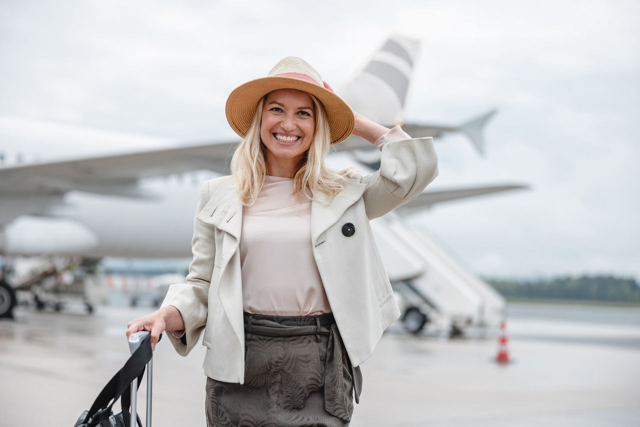 Außenaufnahme einer gutaussehenden Frau, die gerade ein Flugzeug verlässt. Sie lächelt in die Kamera