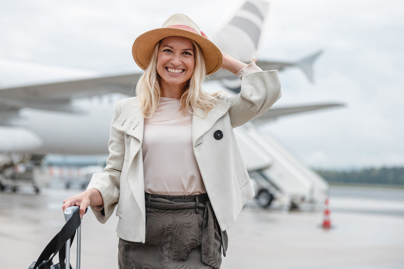 Außenaufnahme einer gutaussehenden Frau, die gerade ein Flugzeug verlässt. Sie lächelt in die Kamera