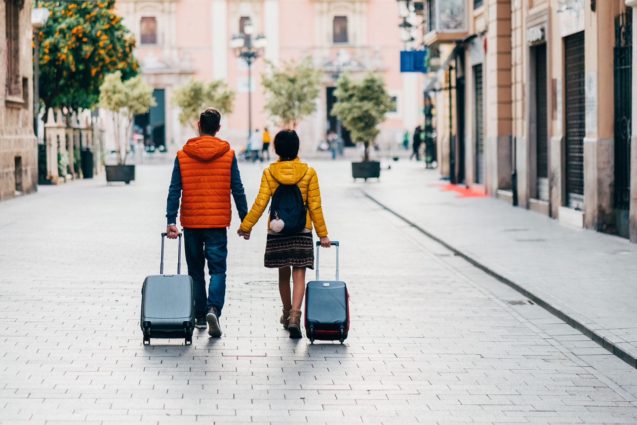 Junges Pärchen mit zwei Koffern Hand in Hand in einer Stadt
