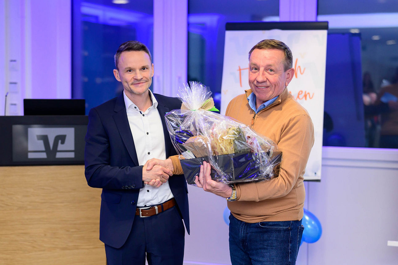 Mann im Anzug übrgibt einem zweiten Mann ein Geschenk.