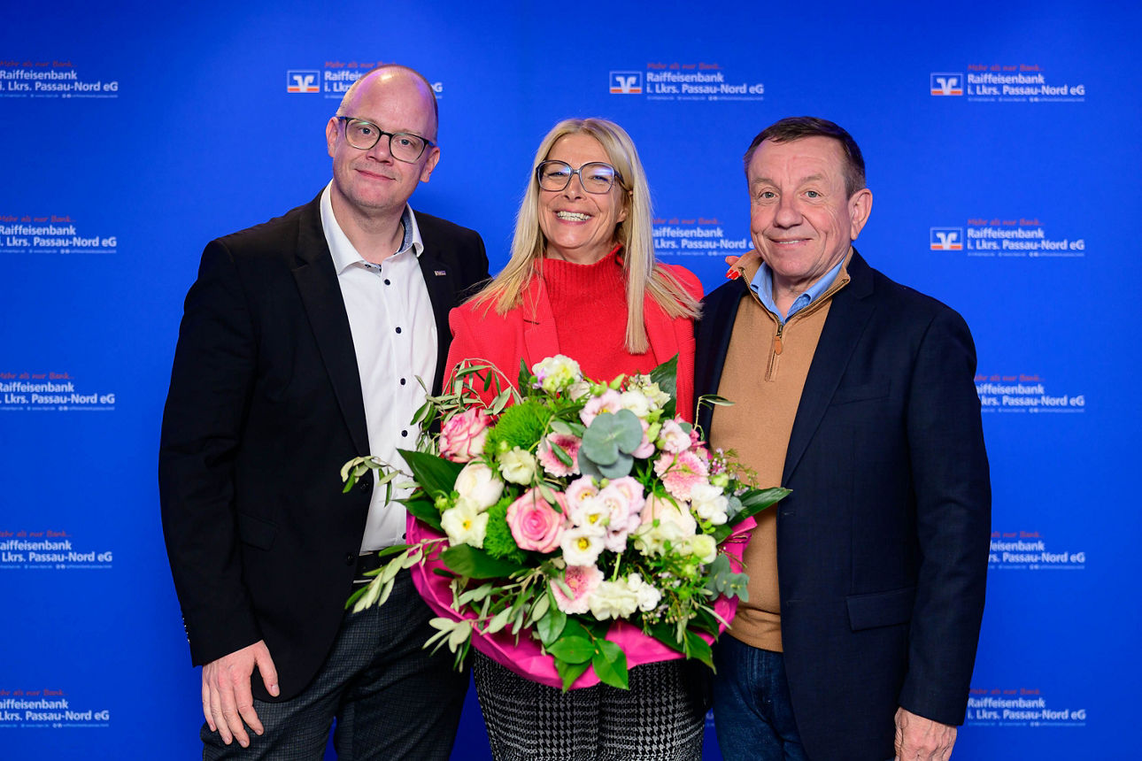 Foto von zwei Männern und einer Frau in der Mitte mit einem Blumenstrauß in den Händen.