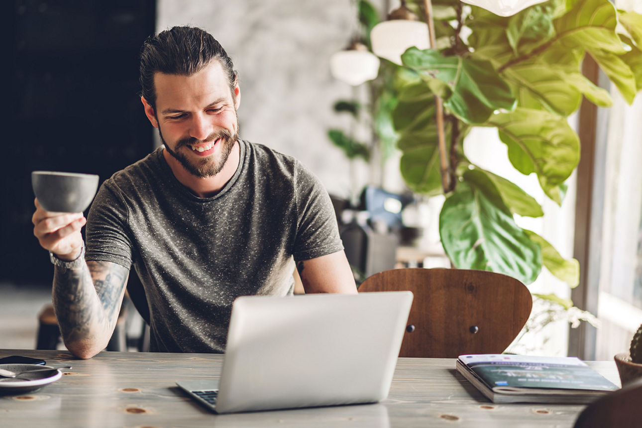 Mann mit Kaffee in der Hand schaut auf Laptop