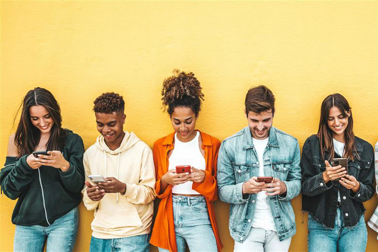 Fünf Jugendliche vor einer gelben Wand am Handy