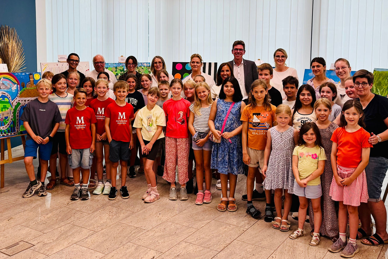 Gruppenfoto von Kindern und Erwachsenen in einem Raum mit mehreren bunten Kunstwerken auf Staffeleien