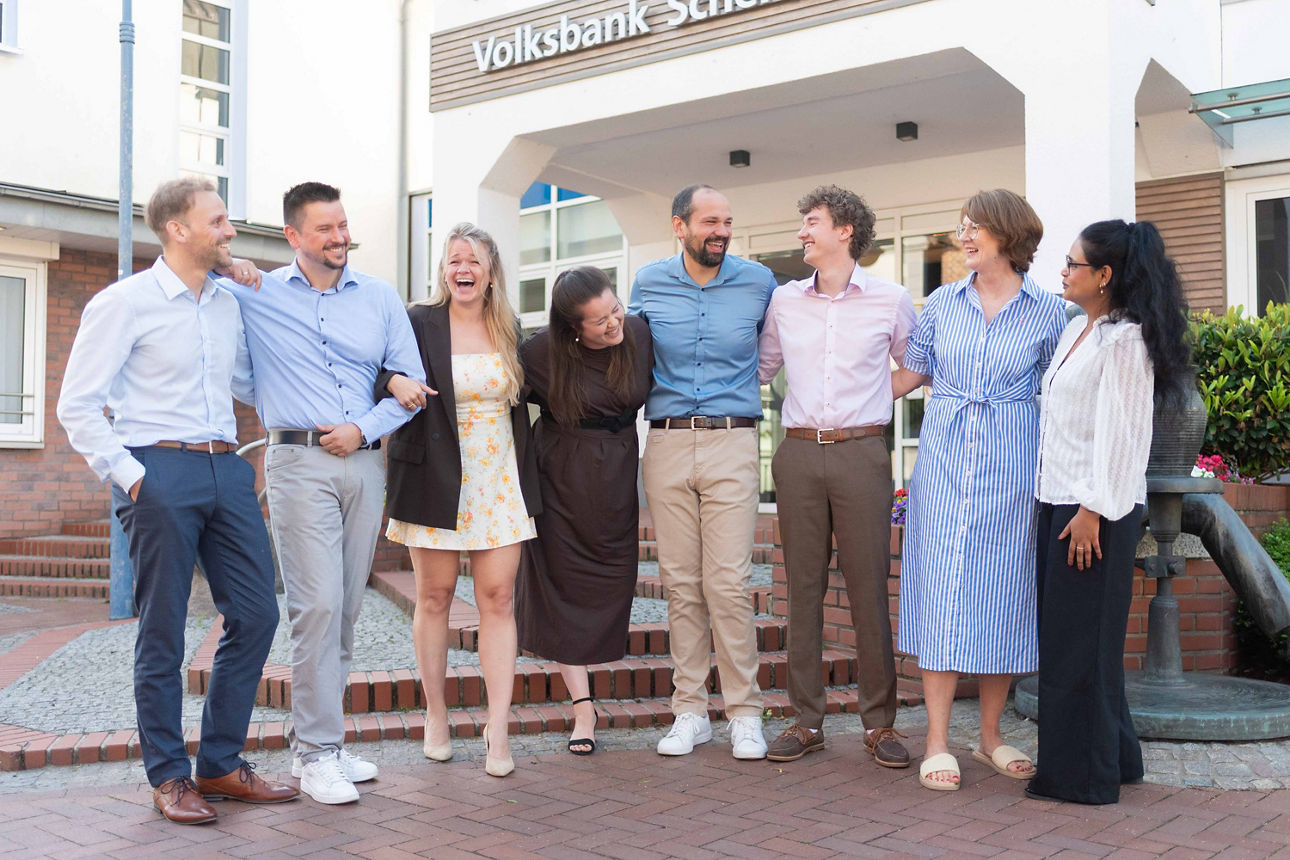 Vier Kollegen und vier Kolleginnen der Volksbank Schermbeck stehen Arm in Arm vor der Bank