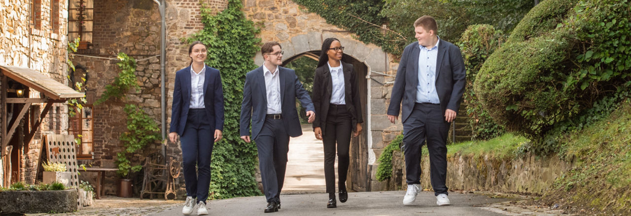 Vier Auszubildende in Business-Kleidung stehen vor einem Tor und lächeln