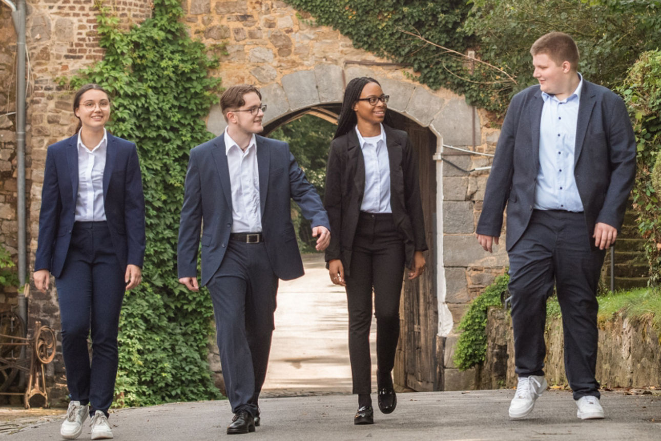 Vier Auszubildende in Business-Kleidung stehen vor einem Tor und lächeln