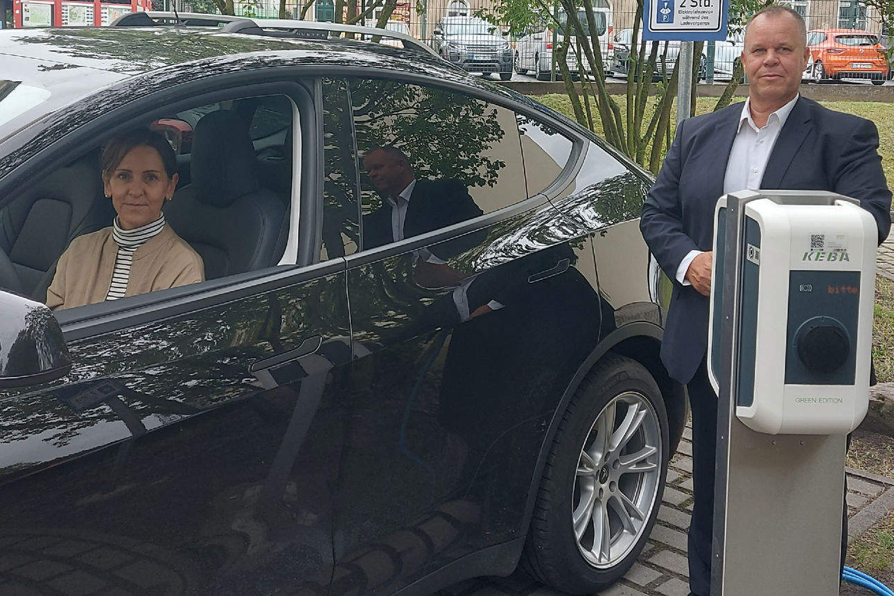 im Auto sitzt eine Person und lächelt aus dem Fenster, eine Person steht vor der Ladesäule