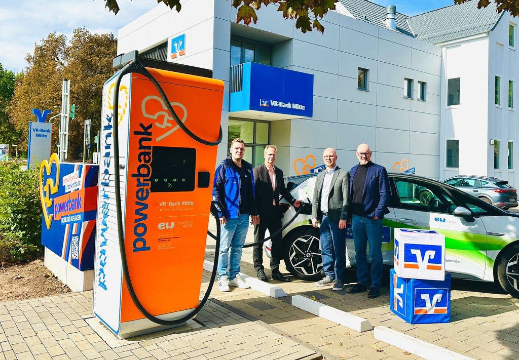 Vier männliche Personen stehen  an einer Ladesäule für Elektro-Autos