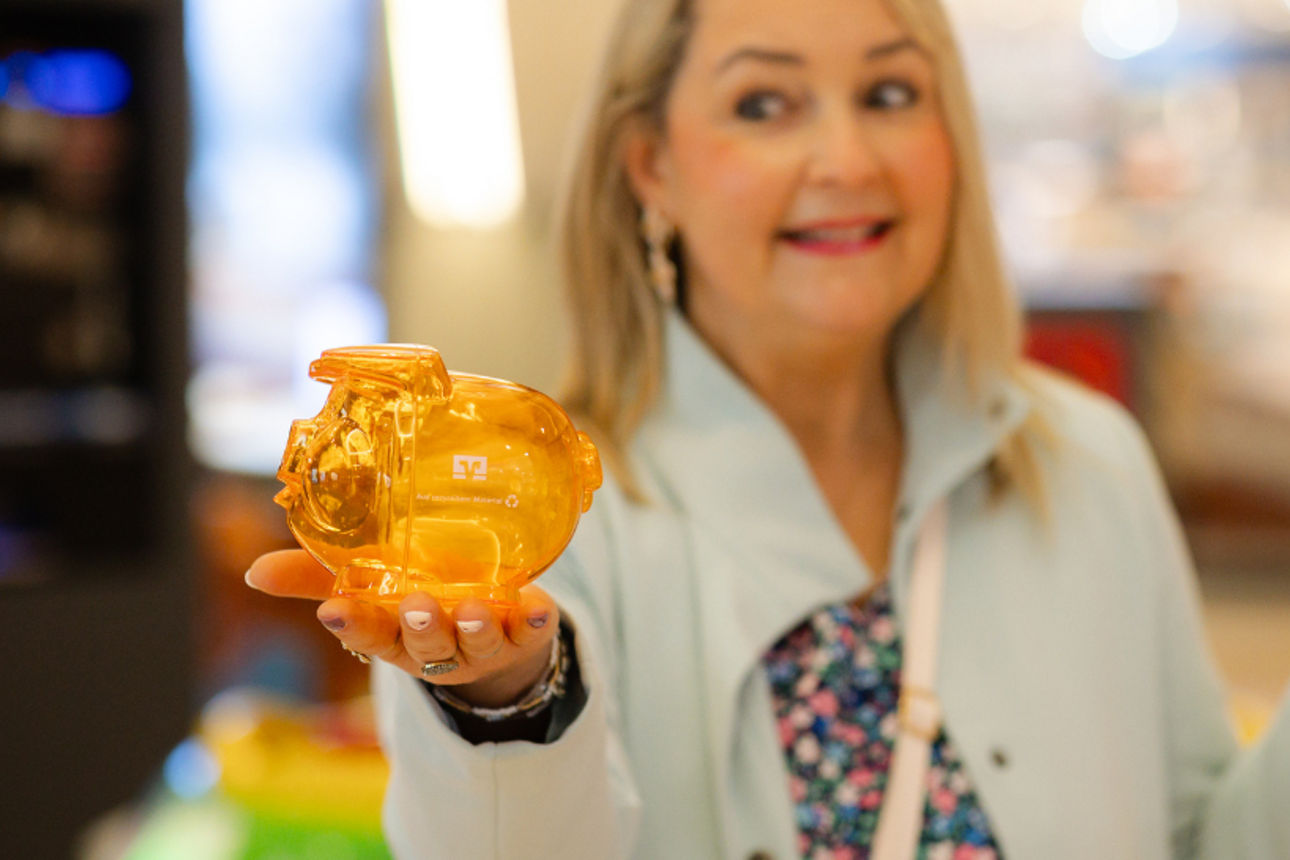 Eine Person hält ein orangefarbenes Sparschwein in der Hand und guckt dieses fragend an.