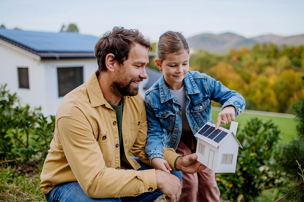 Vater und Tochter halten ein kleines Haus mit Solar-Panel in den Händen