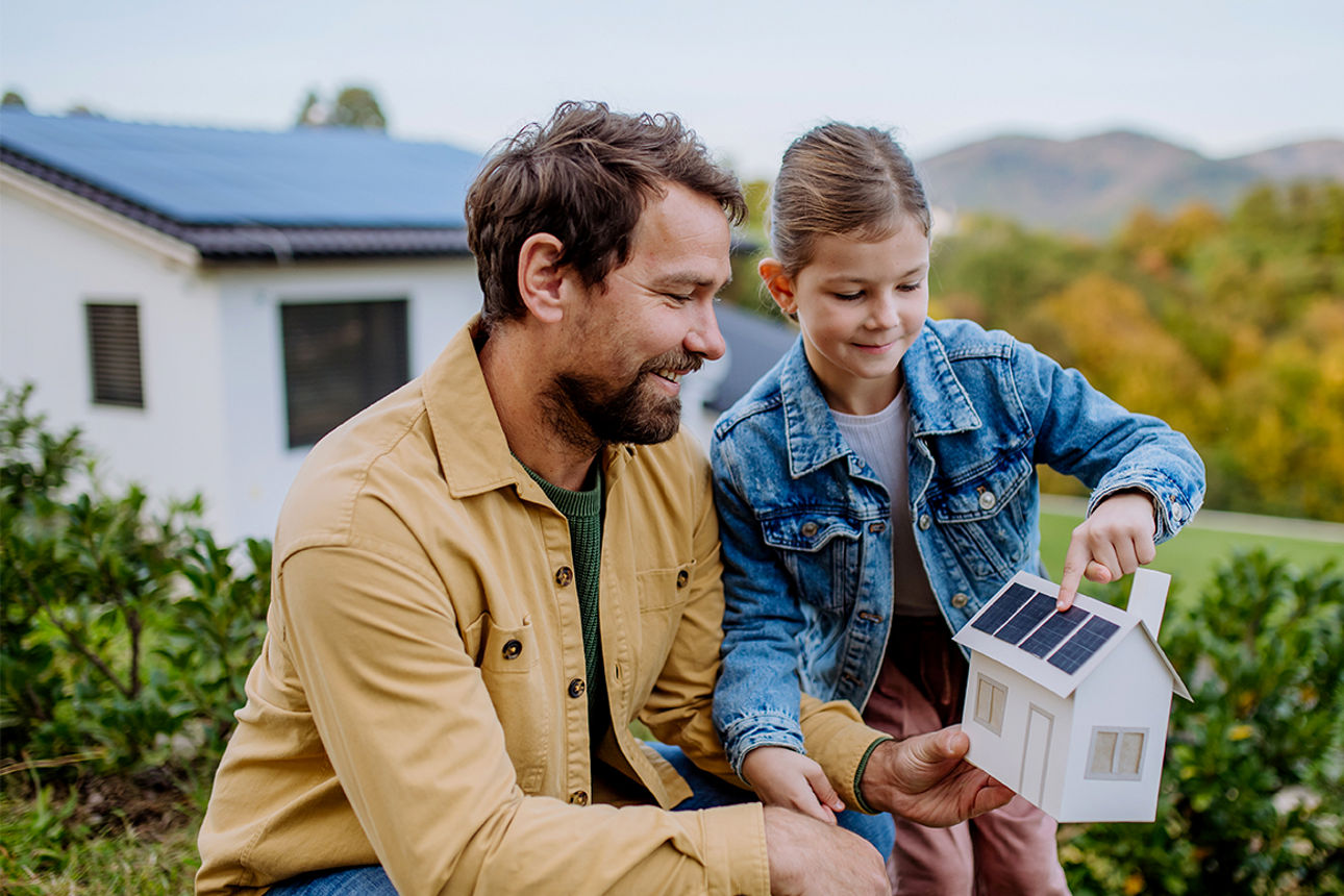 Vater und Tochter halten ein kleines Haus mit Solar-Panel in den Händen