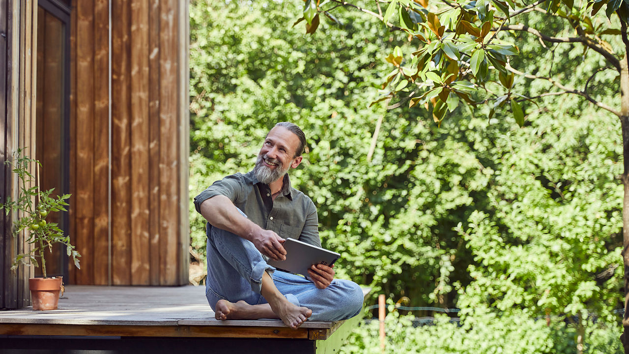 Ein Mann sitzt auf einer Terrasse und hält ein Tablet in der Hand