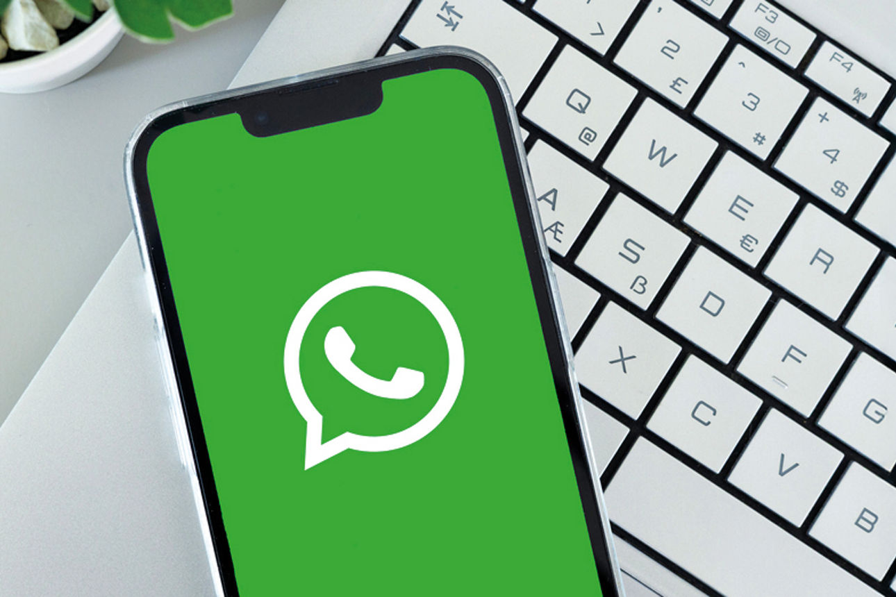 Smartphone mit dem WhatsApp-Logo auf Bildschirm liegt auf Laptop-Tastaur 