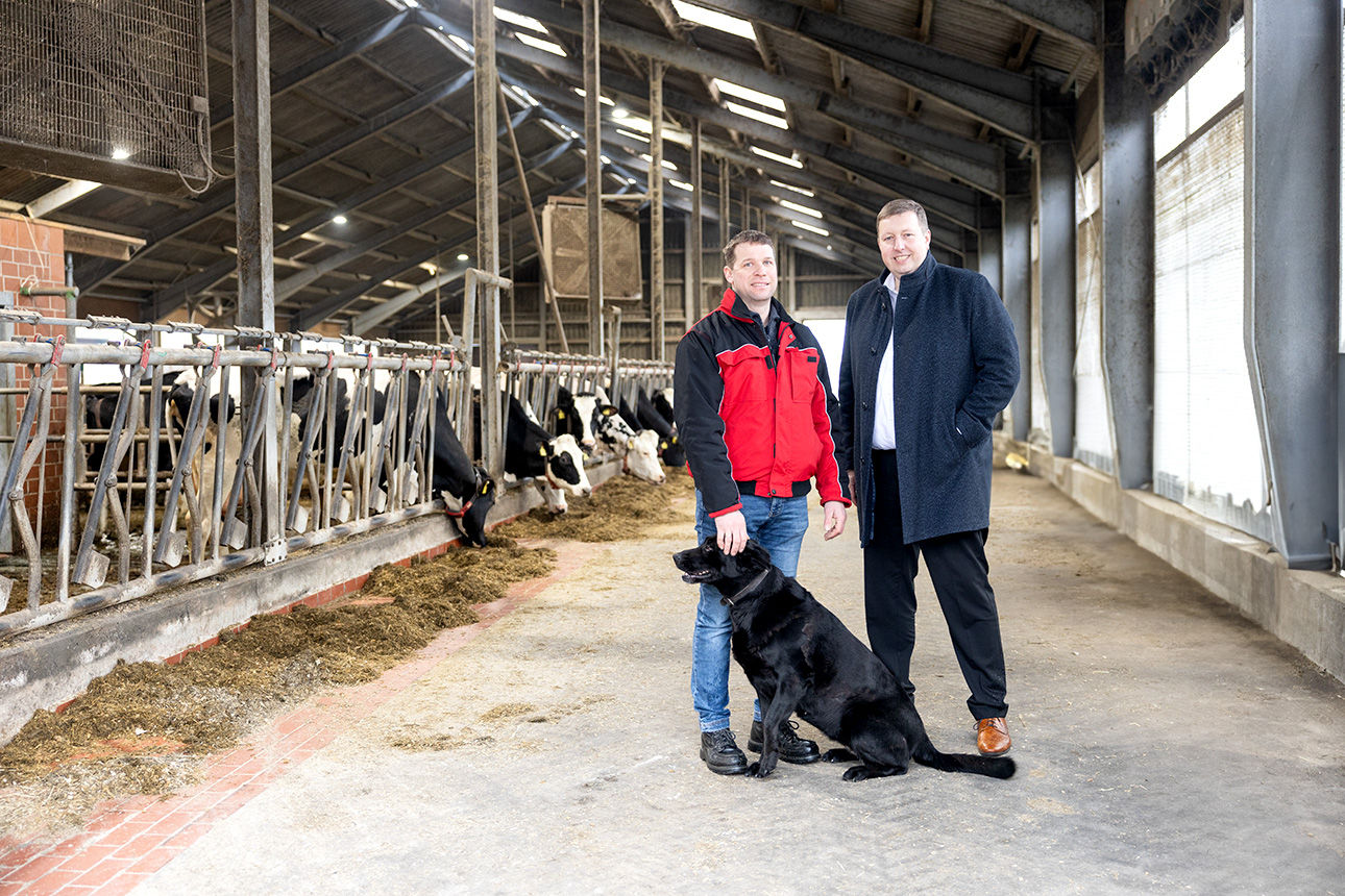 Landwirt mit Hund und Kundenberater stehen in einem Kuhstall