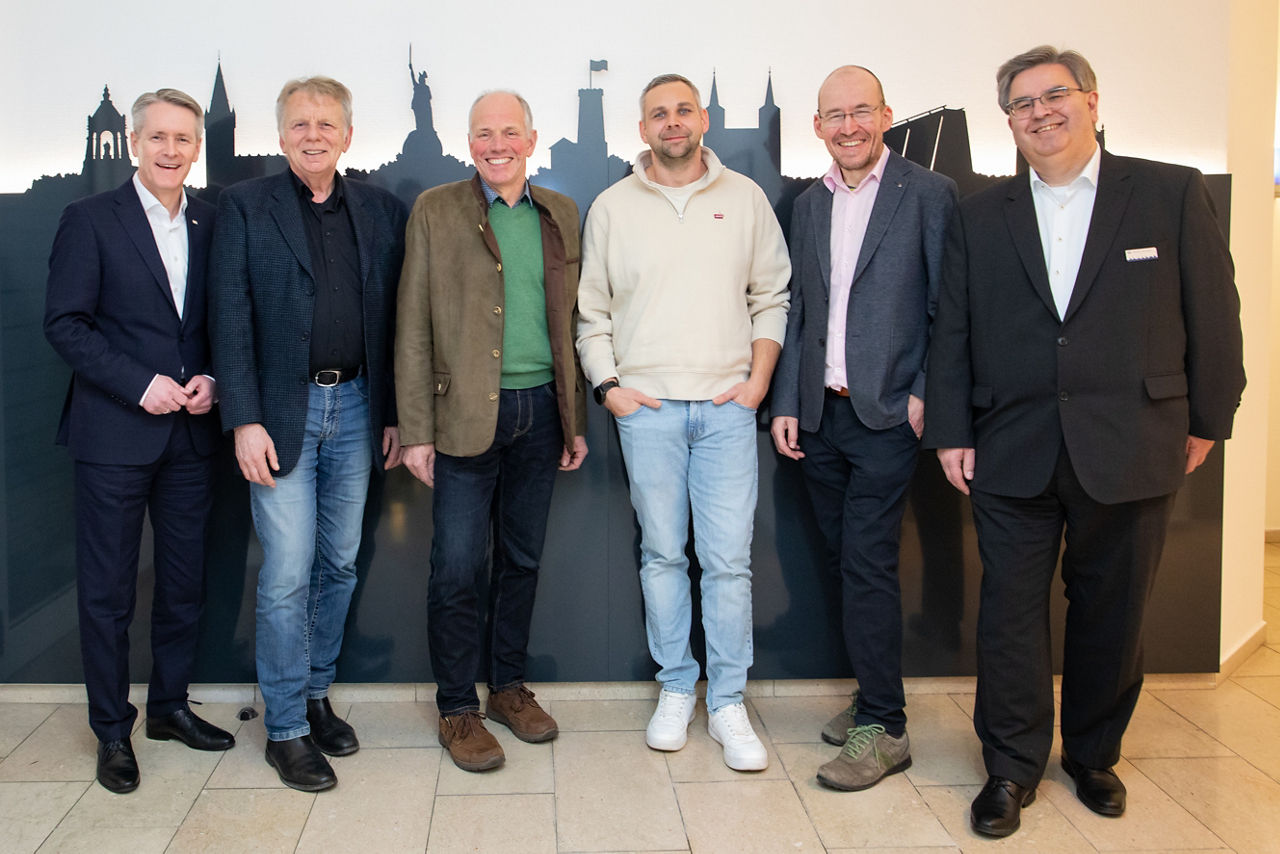  Die Beteiligten der Veranstaltung „Landwirtschaft trifft Volksbank“ im Haus der Immobilie in Detmold stehen vor einer Wand.