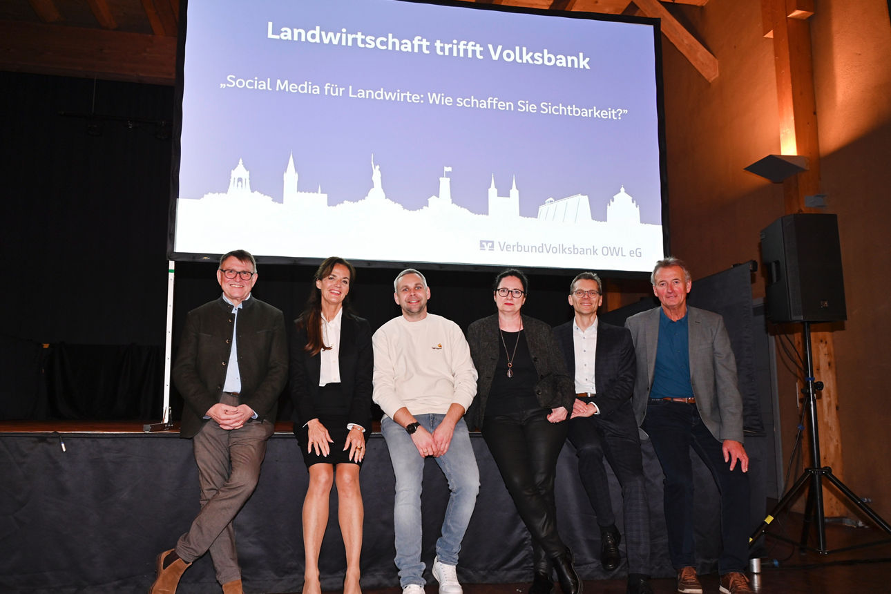 Die Beteiligten der Veranstaltung Veranstaltung „Landwirtschaft trifft Volksbank“ im KuStall in Höxter-Ottbergen lehnen vor einer Bühne. 