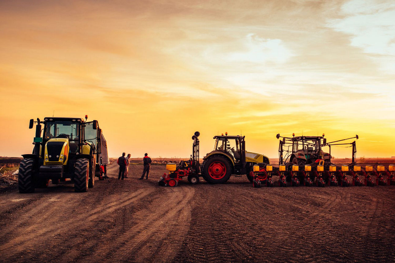 Feld im Sonnenuntergang mit 3 Traktoren und 2 Menschen, die arbeiten