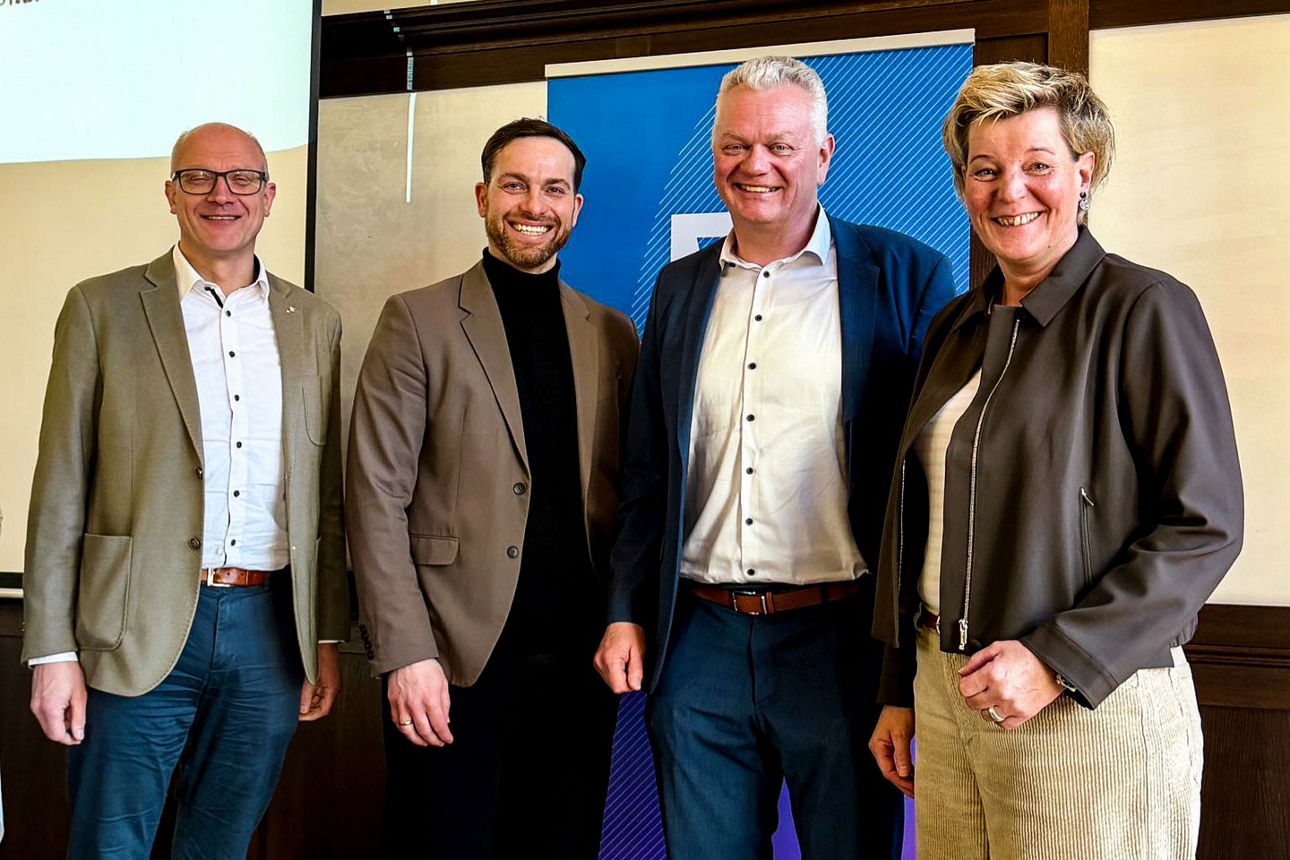 Vier Personen stehen nebeneinander und schauen lächelnd in die Kamera