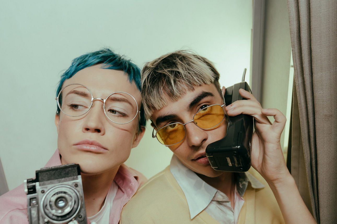 Mann und Frau halten ein altes Telefon und eine alte Kamera vor sich