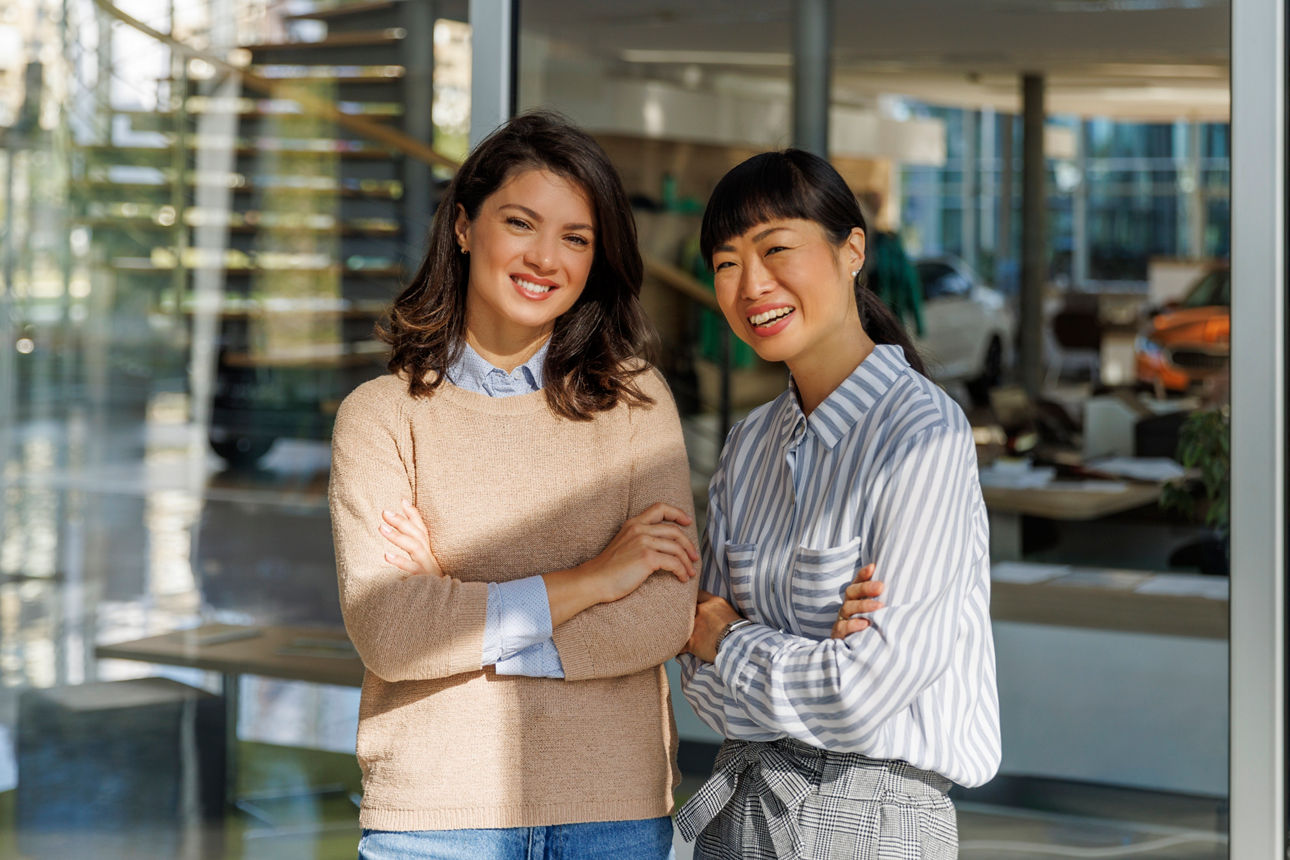 Zwei Frauen stehen vor einer Glaswand und lächeln