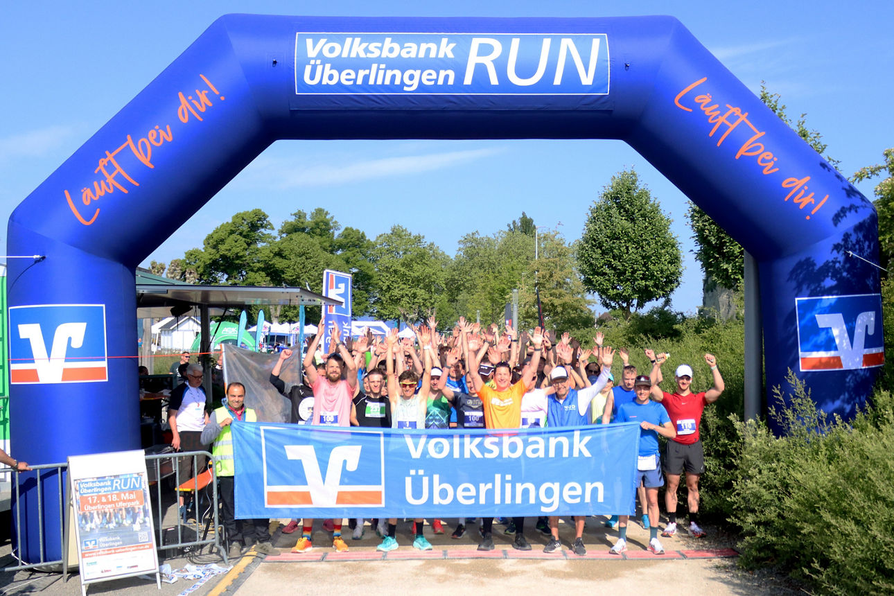 Viele Läuferinnen und Läufer stehen am Startbogen des Volksbank Überlingen RUN und freuen sich mit hochgestreckten Händen