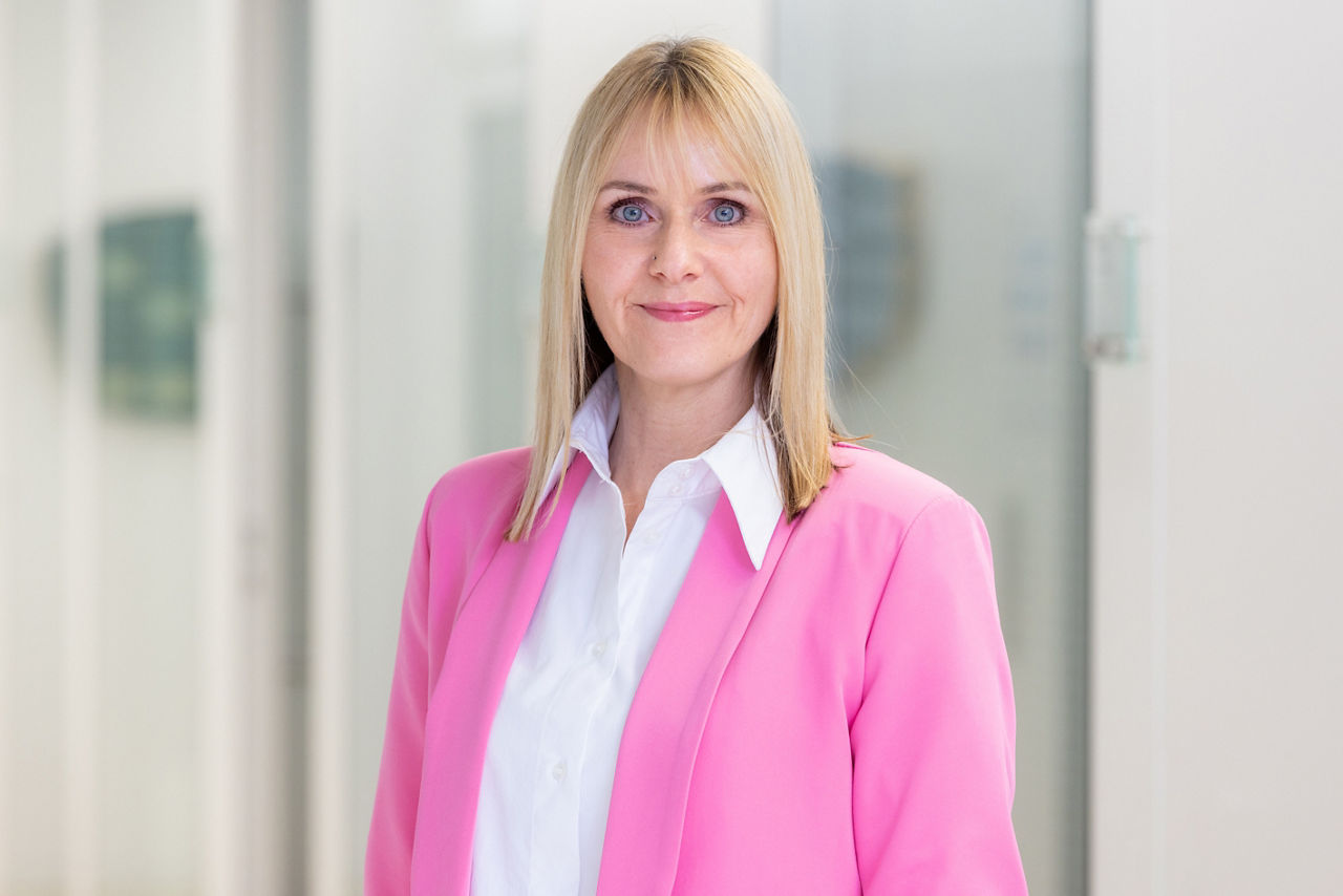 Eine Frau mit Anzug mit einem Büro im Hintergrund. 