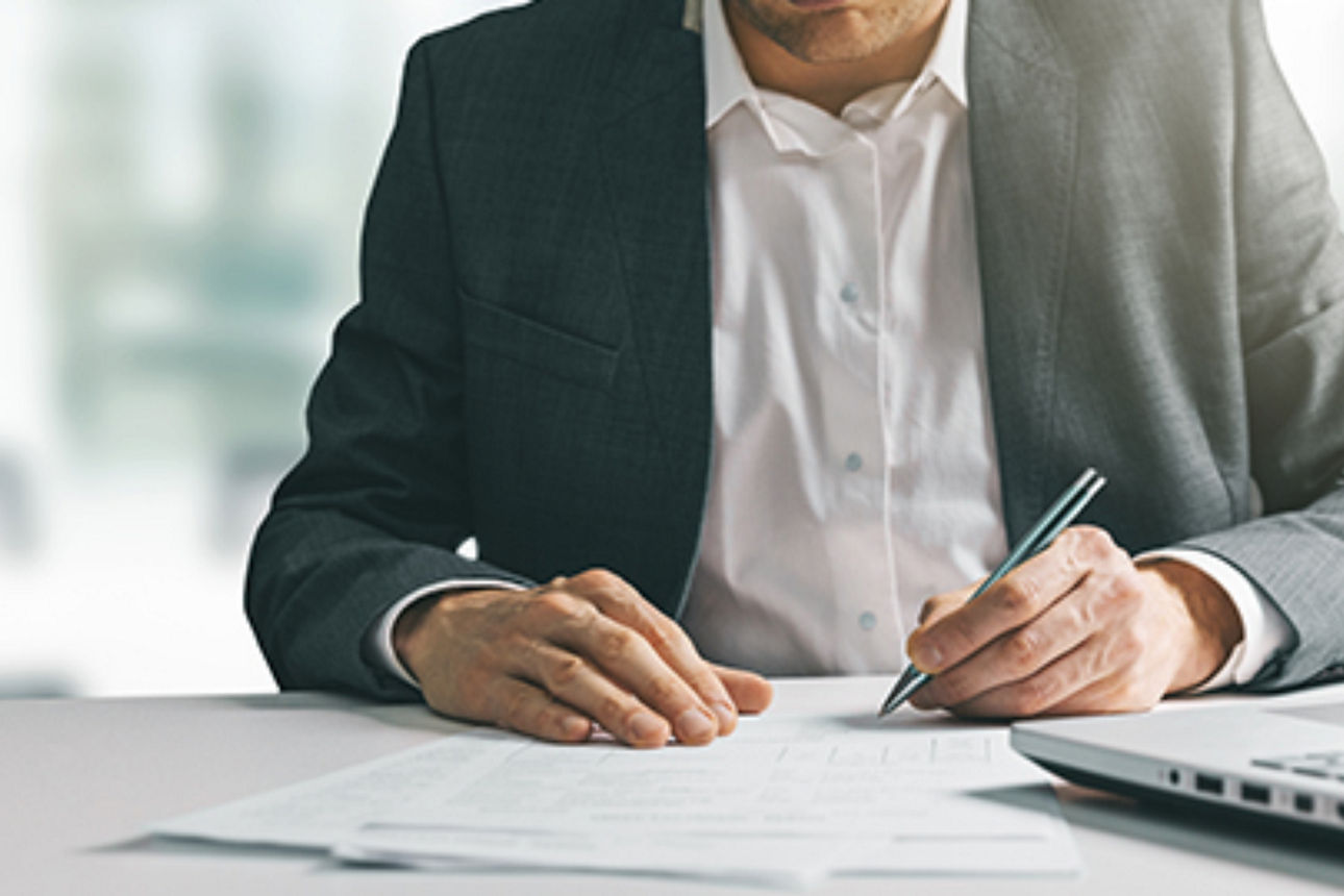 Ein Mann im Anzug arbeitet konzentriert an seinem Laptop an einem gut organisierten Schreibtisch.