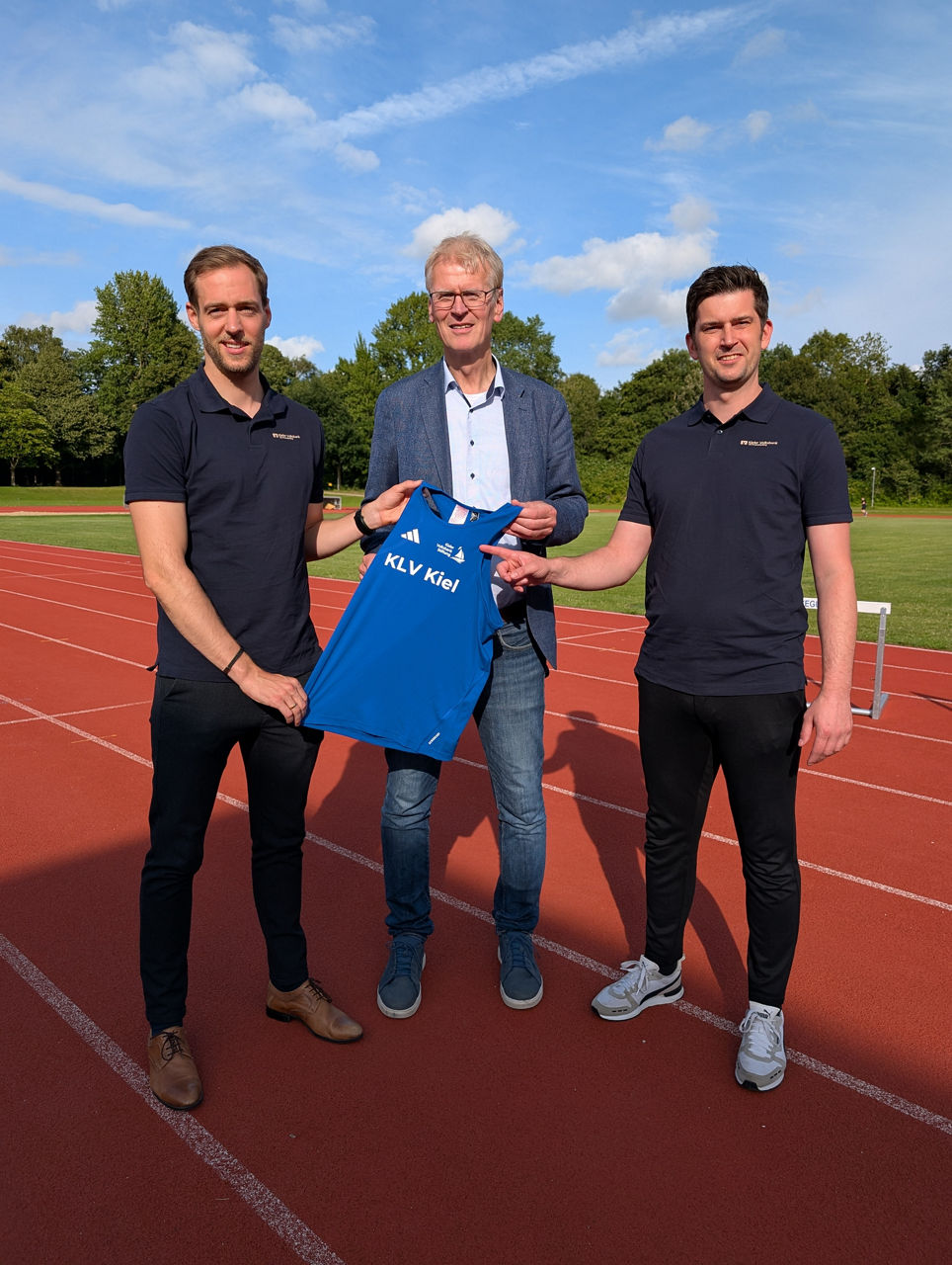 drei Männer halten ein blaues Trikot in den Händen