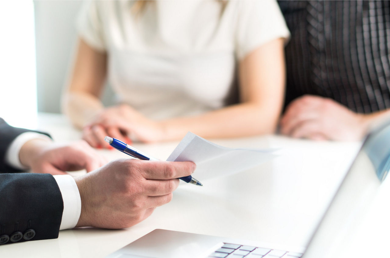 Die Hand eines Beraters hält einen Kugelschreiber und einen Vertrag auf dem Tisch.