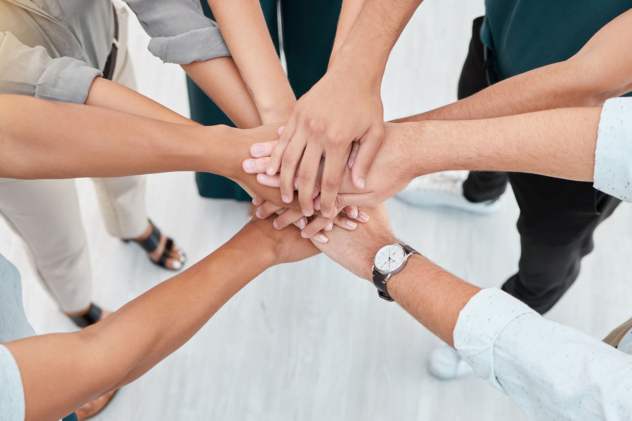 Eine Gruppe von Menschen steht im Kreis und hält eine Hand in die Mitte.