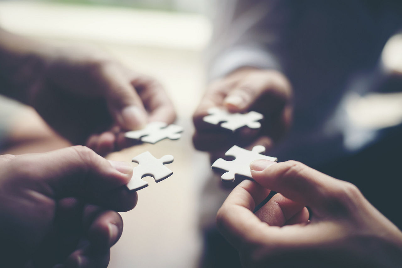 Vier einzelne Hände die jeweils ein Puzzelteil halten