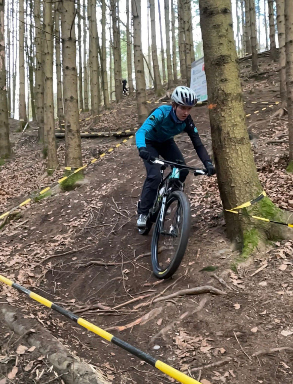 Mountainbike-Fahrer auf einem schmalen Waldtrail zwischen Bäumen, während einer Abfahrt auf unebenem, wurzeligem Gelände.