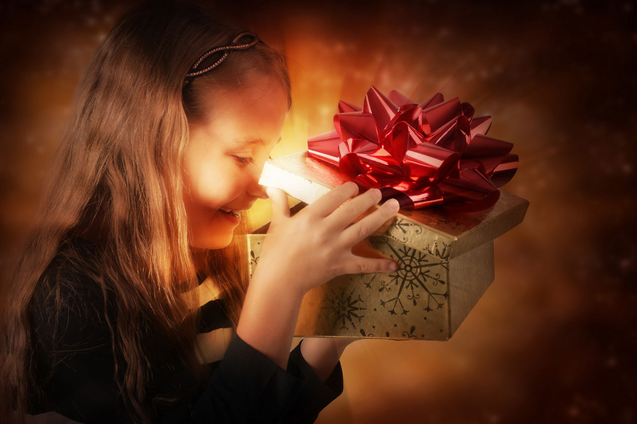 Leuchtende Kinderaugen: kleines Mädchen mit langen blonden Haaren öffnet einen Geschenkkarton mit roter Schleife