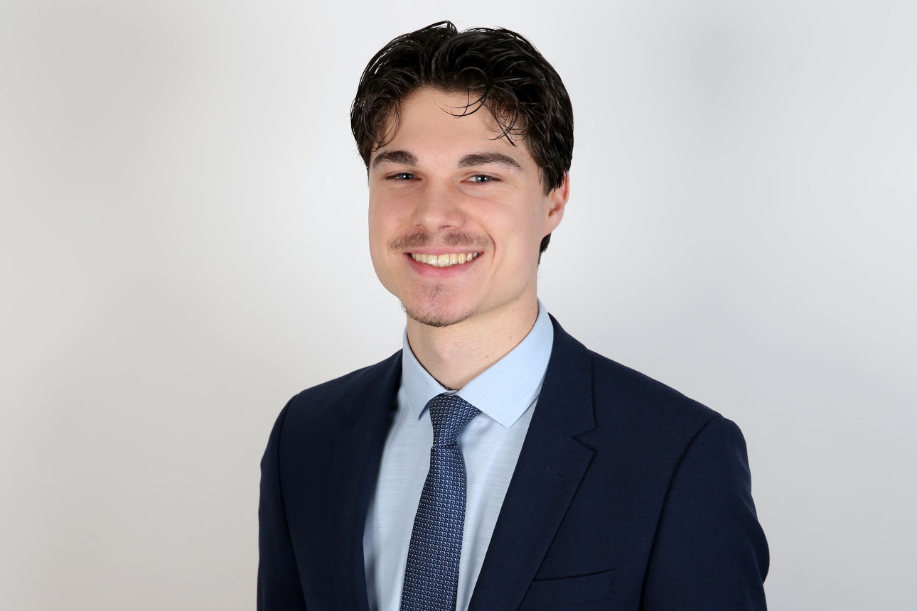 Ein lächelnder Mann in einem Anzug schaut in die Kamera.