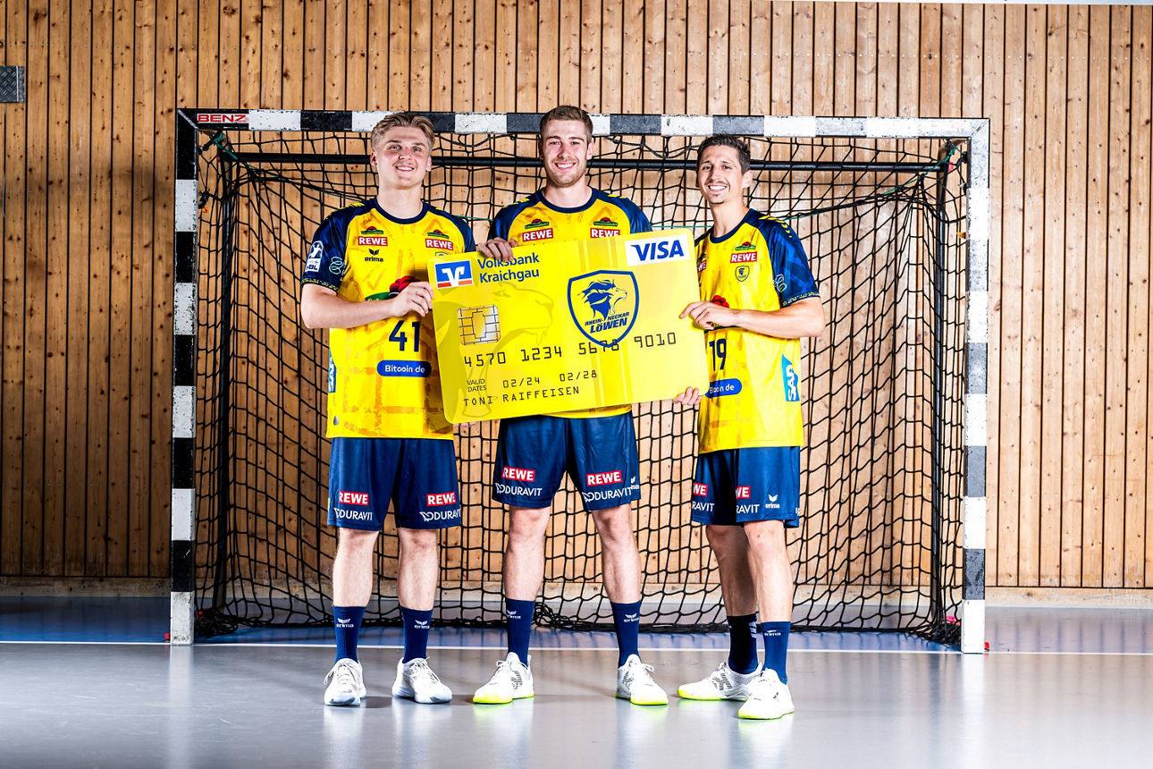 Drei Spieler der Rhein Neckar Löwen halten eine große Kreditkarte im Löwen-Design. | Fotograf: Max Krause