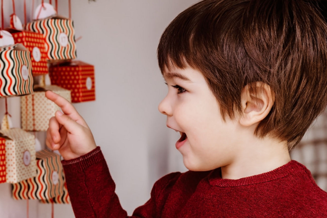 Ein Junge zeigt lächelnd auf seinen Adventskalender