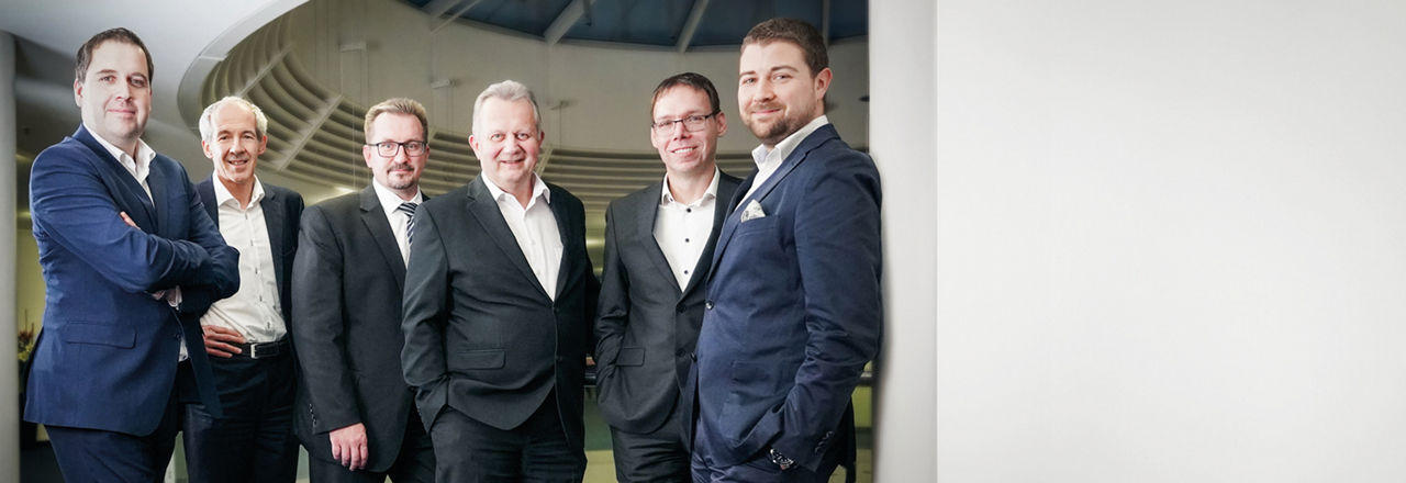 fünf Männer in Anzügen, die in einem modernen Büro zusammenstehen
