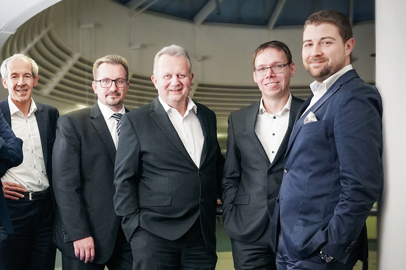  fünf Männer in Anzügen, die in einem modernen Büro zusammenstehen