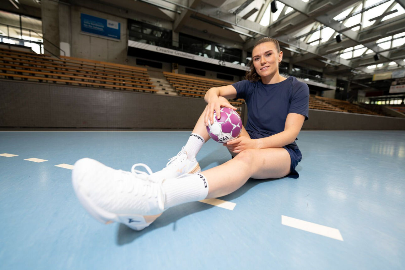 Frau mit Handball sitzt auf dem Boden einer Sporthalle